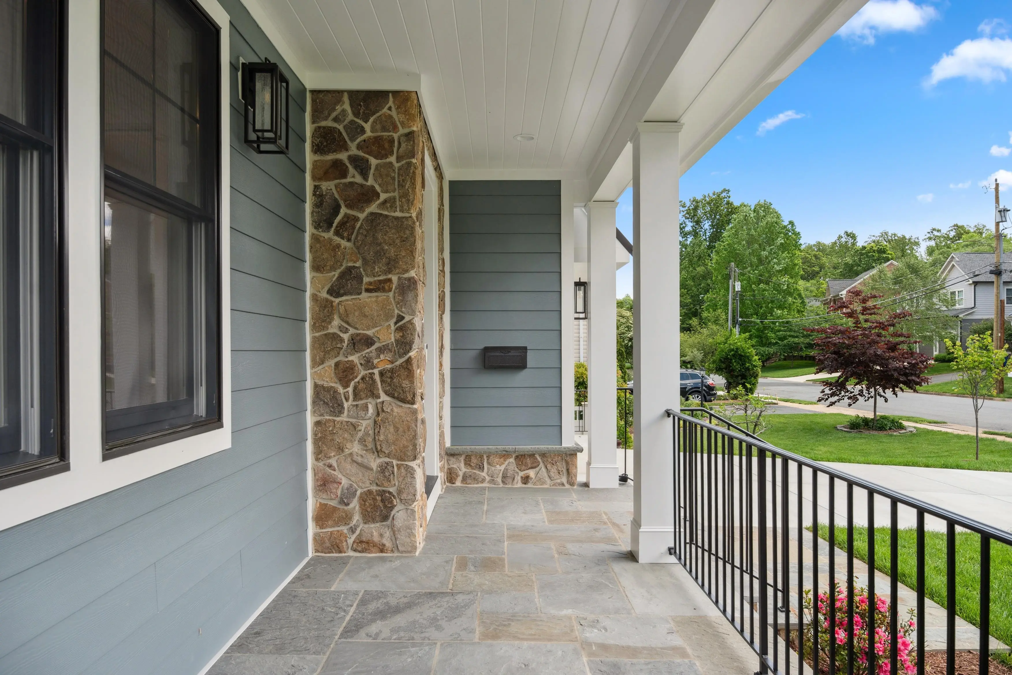 Real estate exterior photography of a charming front porch entry with stone columns and blue siding in the DC Maryland Virginia area