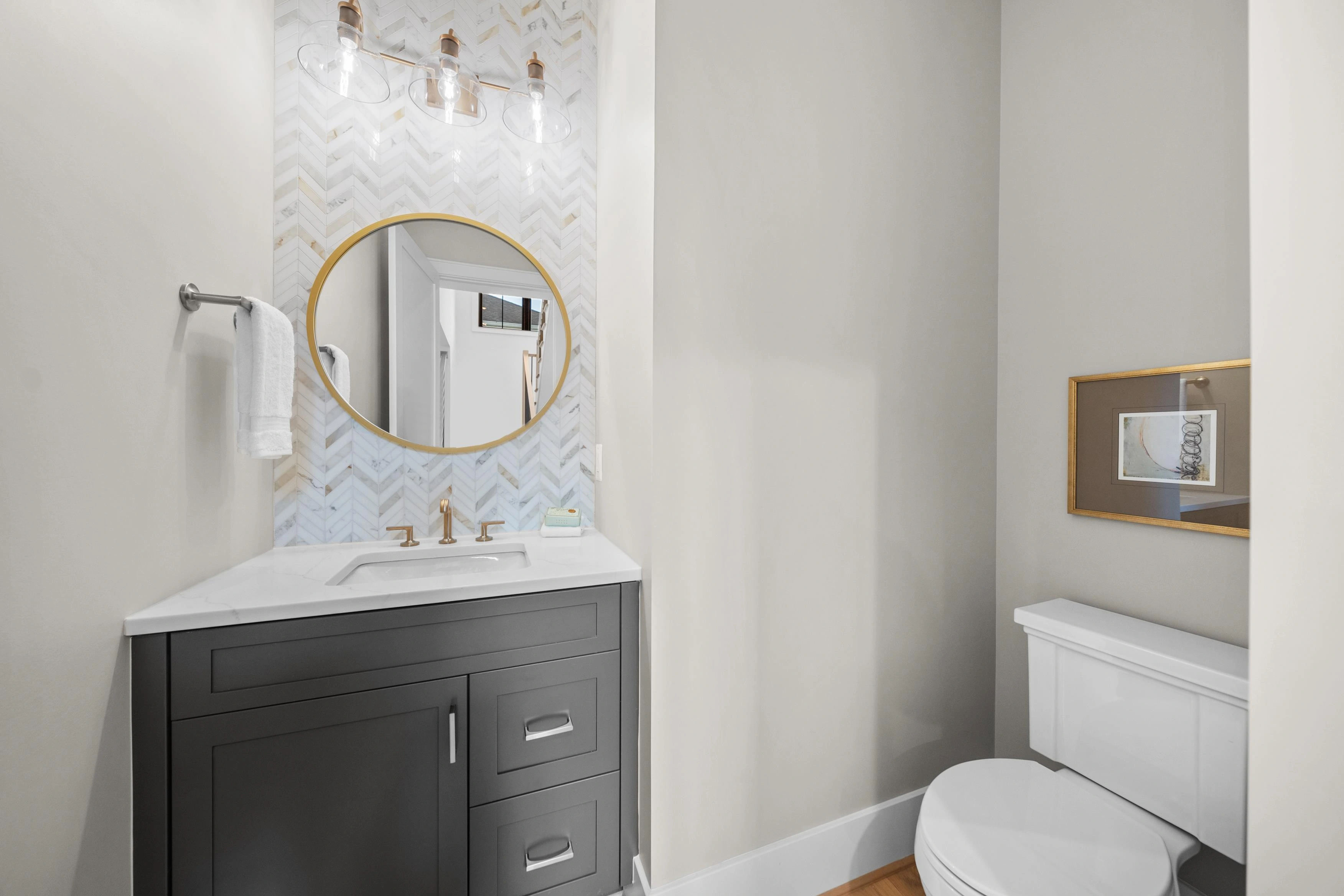 Powder room with herringbone marble accent wall, gold-framed round mirror, and glass pendant lighting