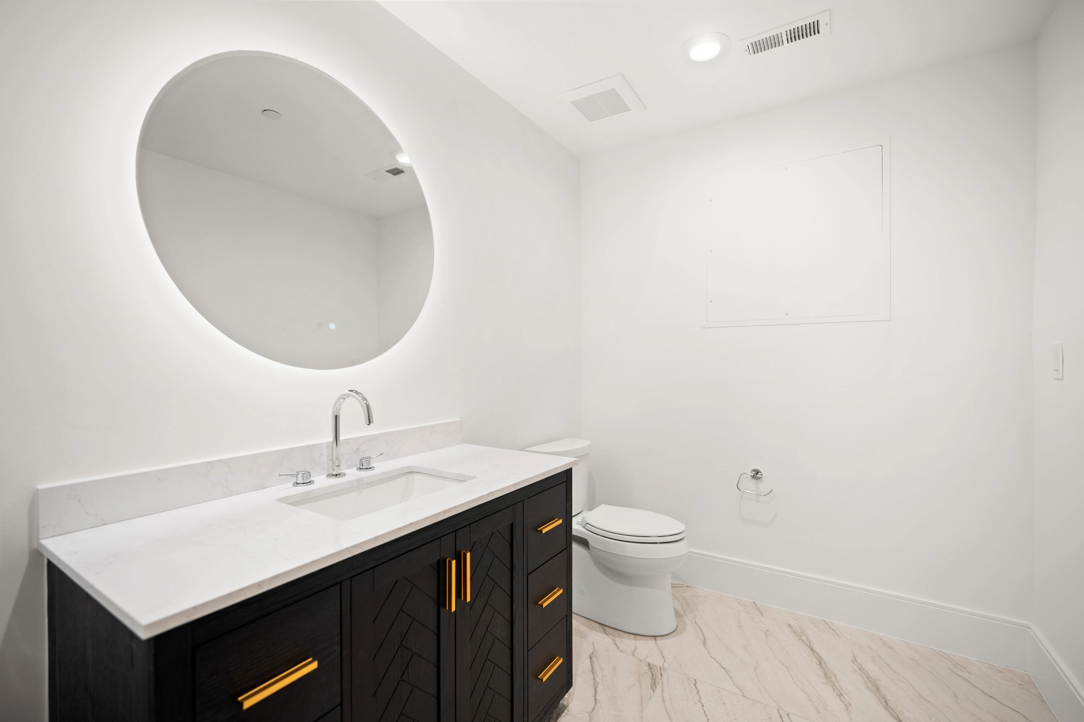 Basement powder room with round backlit mirror, black chevron-pattern vanity, and gold hardware