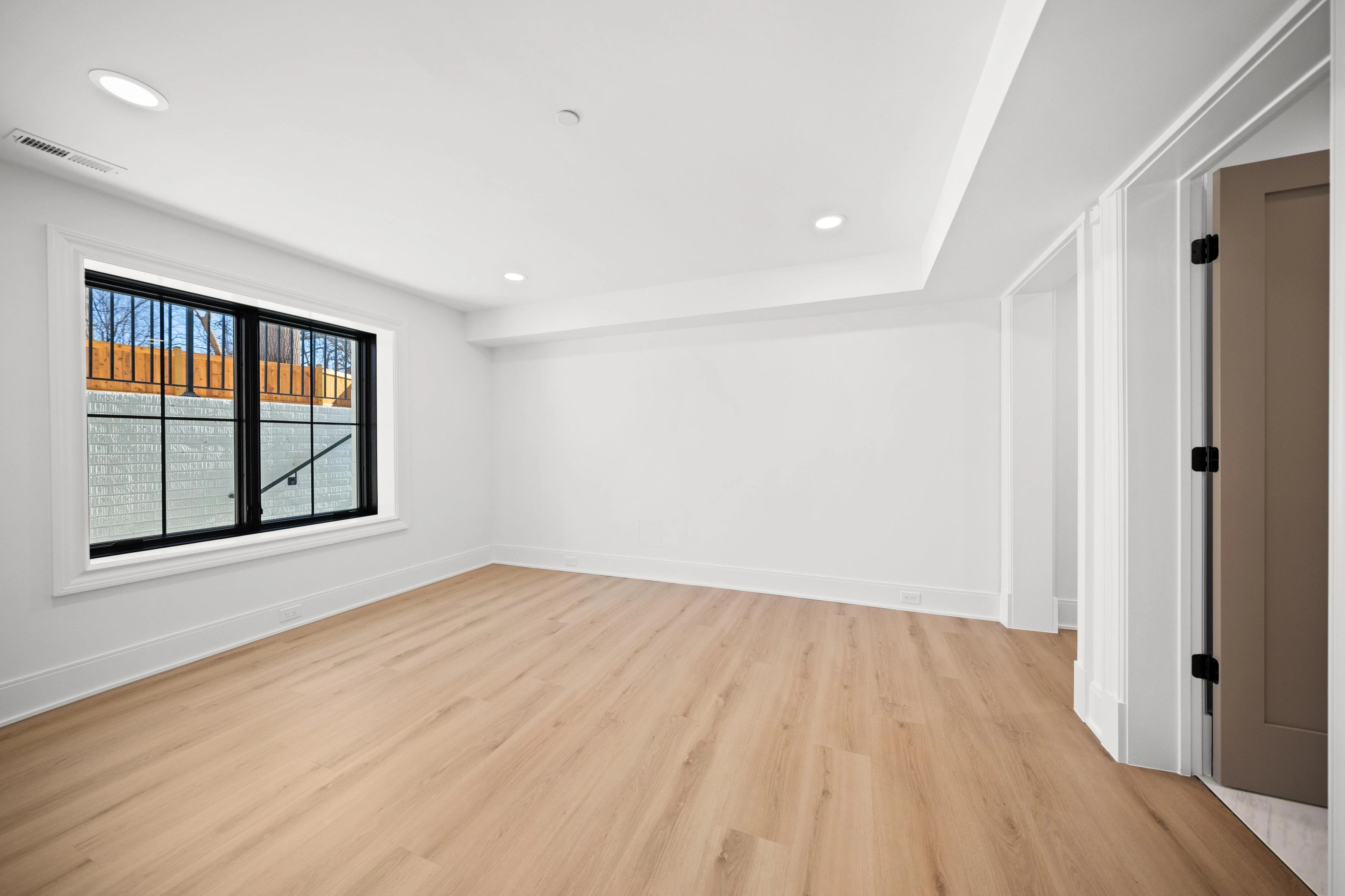 Finished basement with open layout, iron staircase railing, glass French door to patio, and LVP flooring
