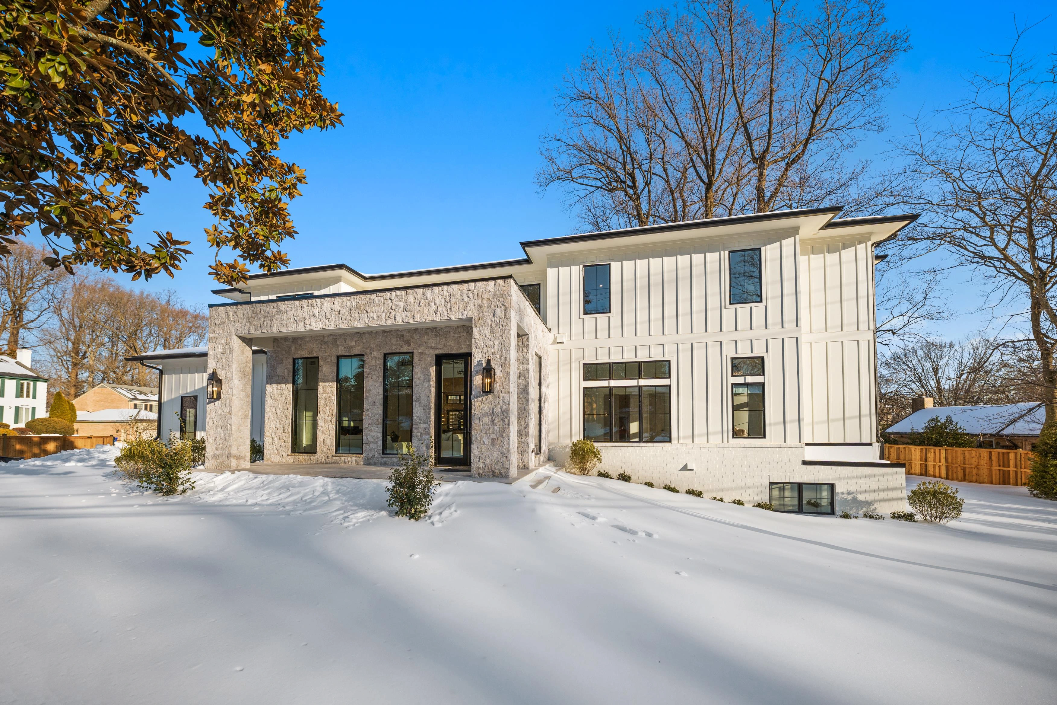 Rear elevation of three-story luxury home with white siding, black windows, and fenced yard in winter