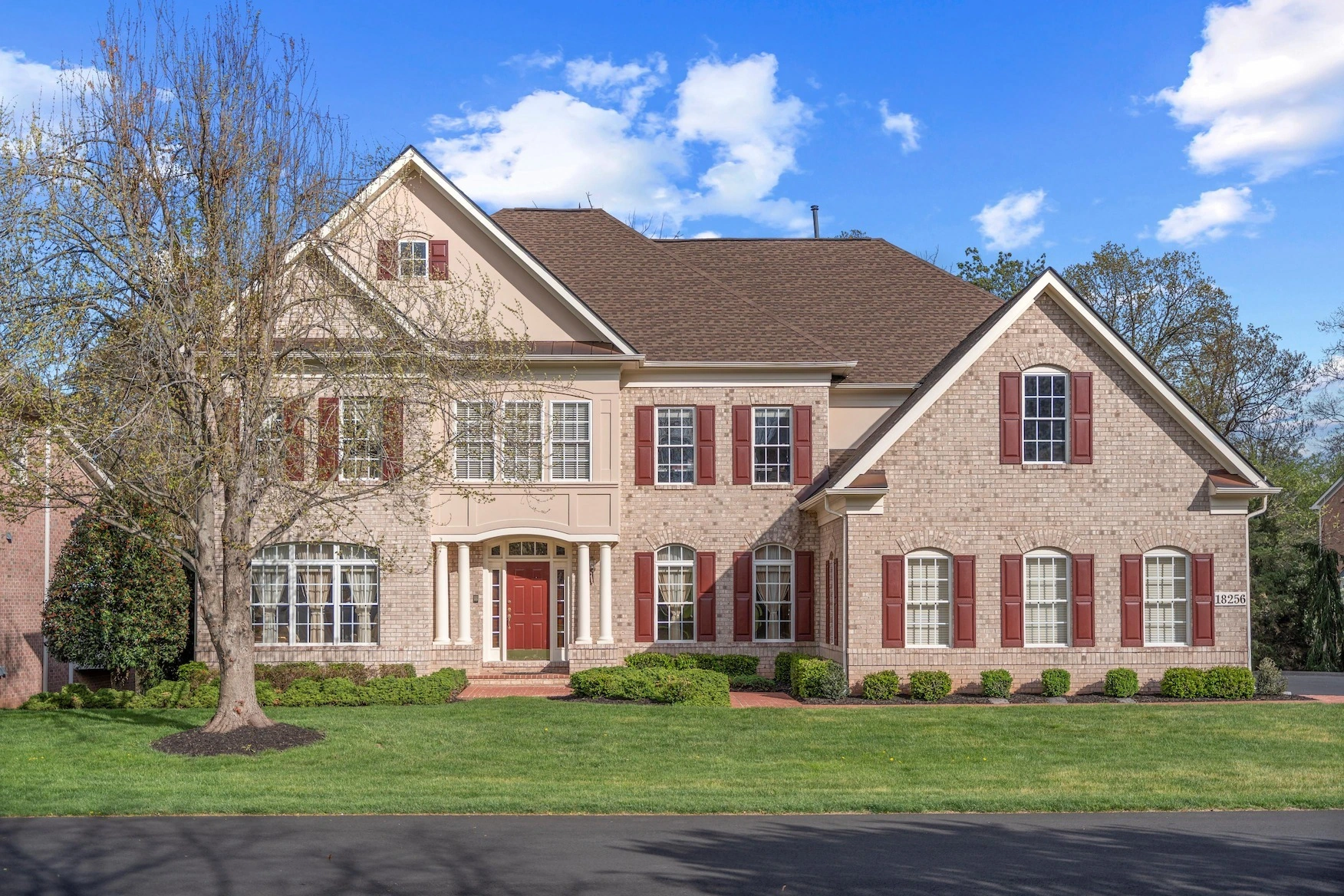 Classic brick colonial home with red shutters and landscaped yard