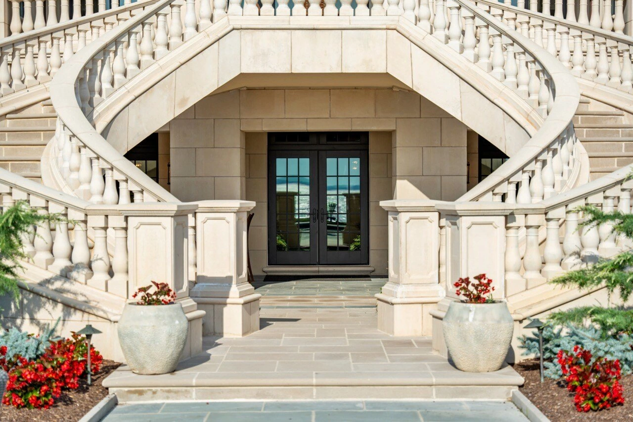 Grand entrance to luxury estate with dual curved stone staircases and iron-glass doors