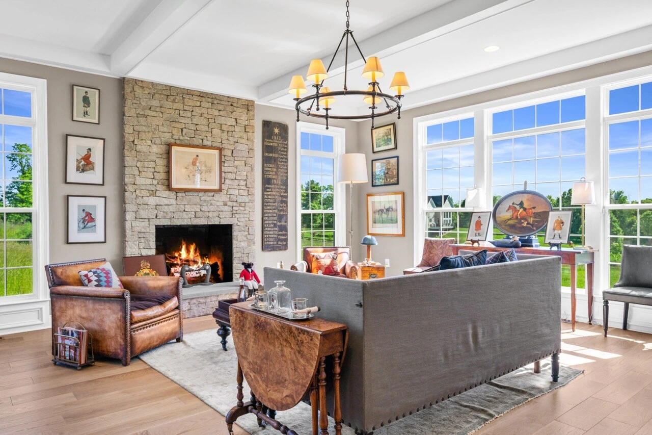 Grand living room with stone fireplace, chandelier, leather seating, and panoramic windows in equestrian estate
