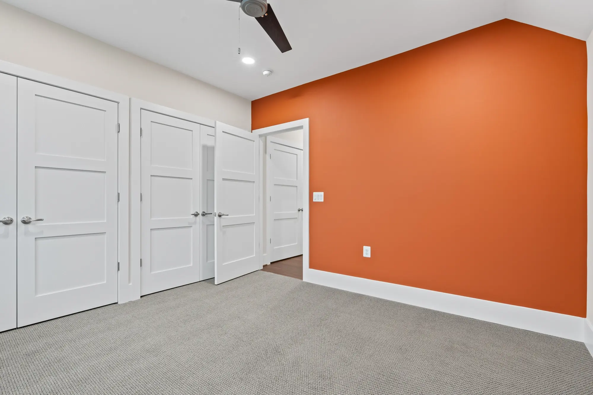 Guest bedroom with bold orange accent wall, carpet, and double closets