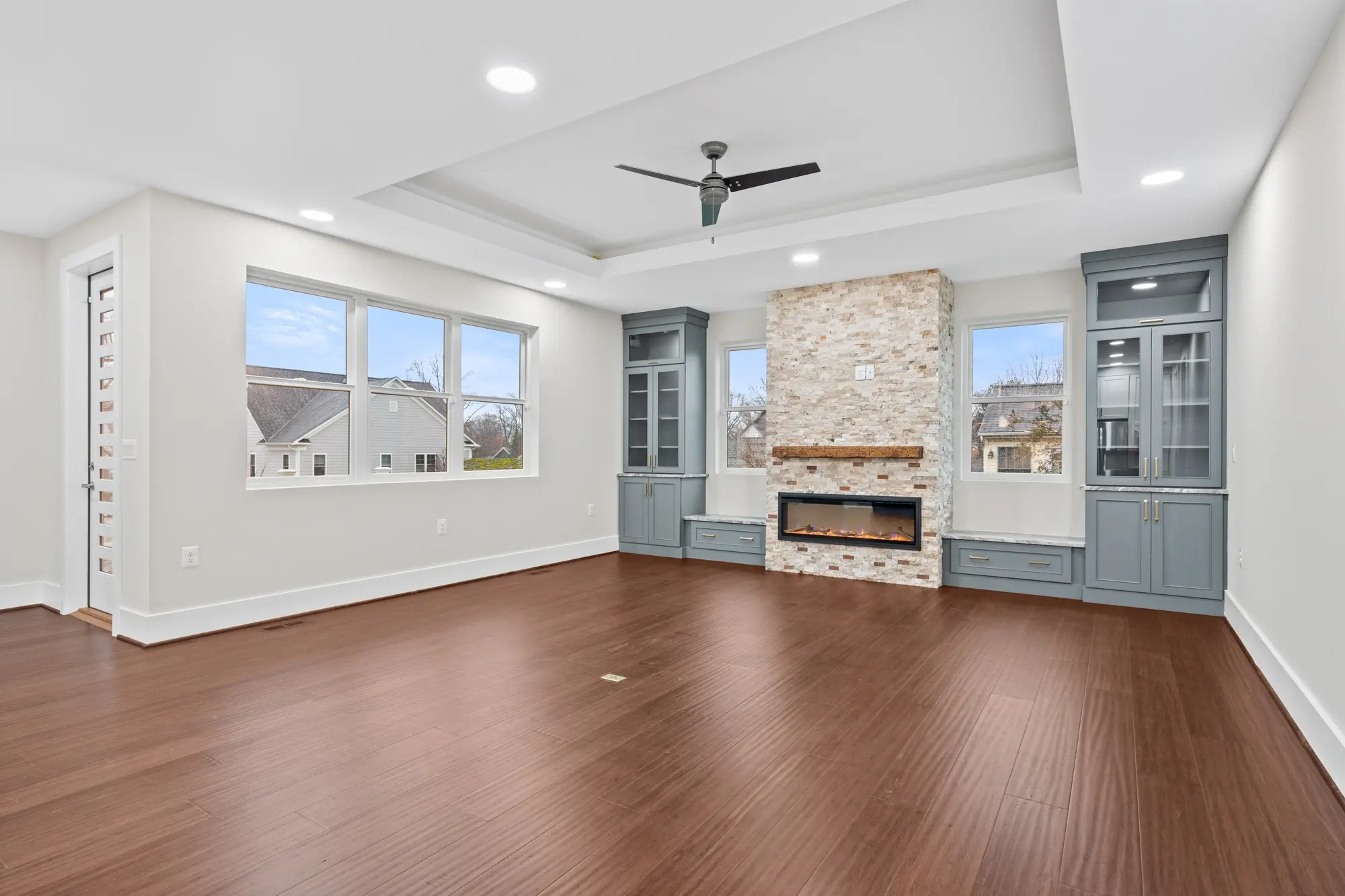 Spacious family room with tray ceiling, stone fireplace, and blue built-in cabinetry
