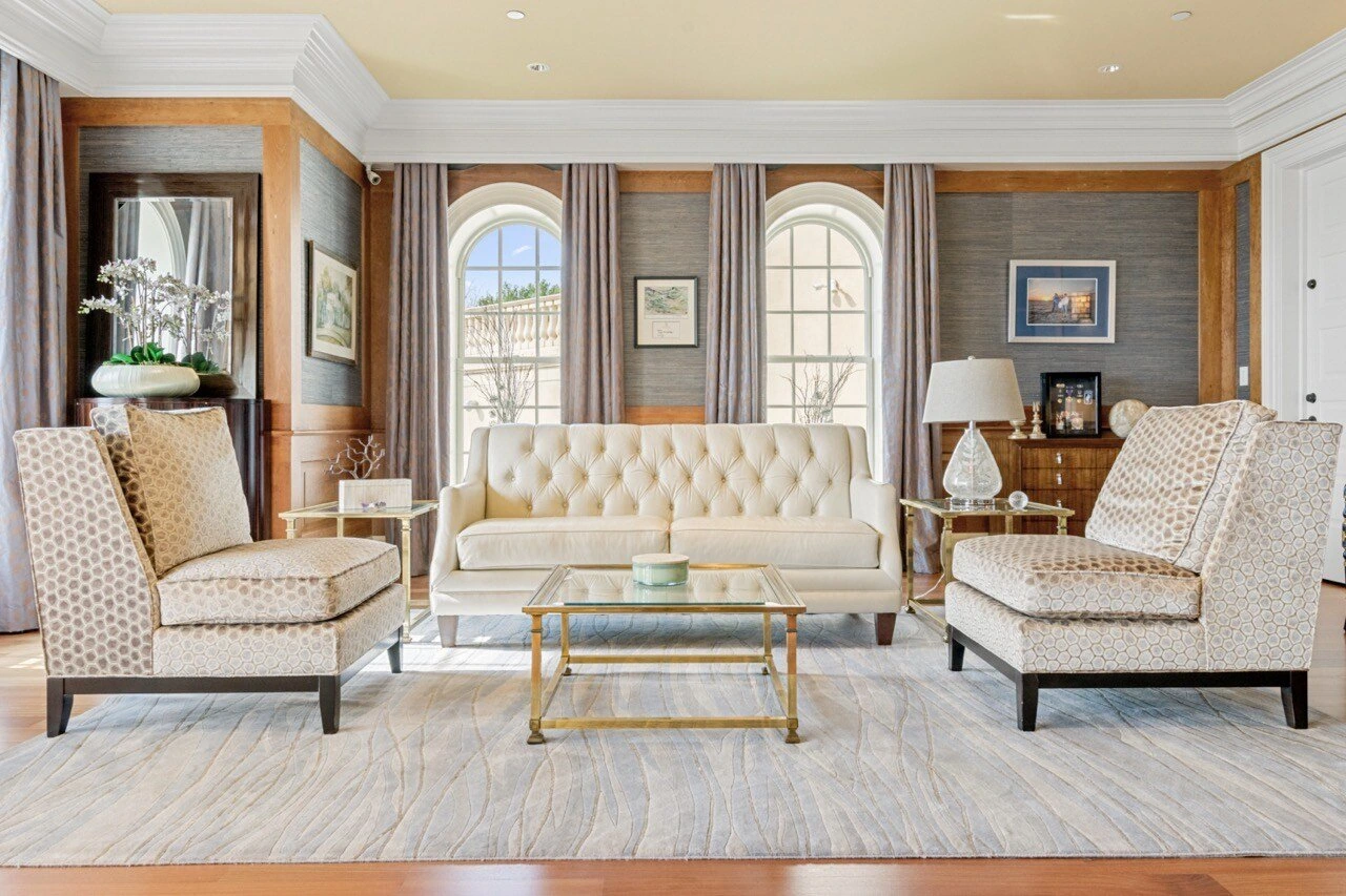 Formal living room with tufted sofa, arched windows, grasscloth walls, and elegant drapery