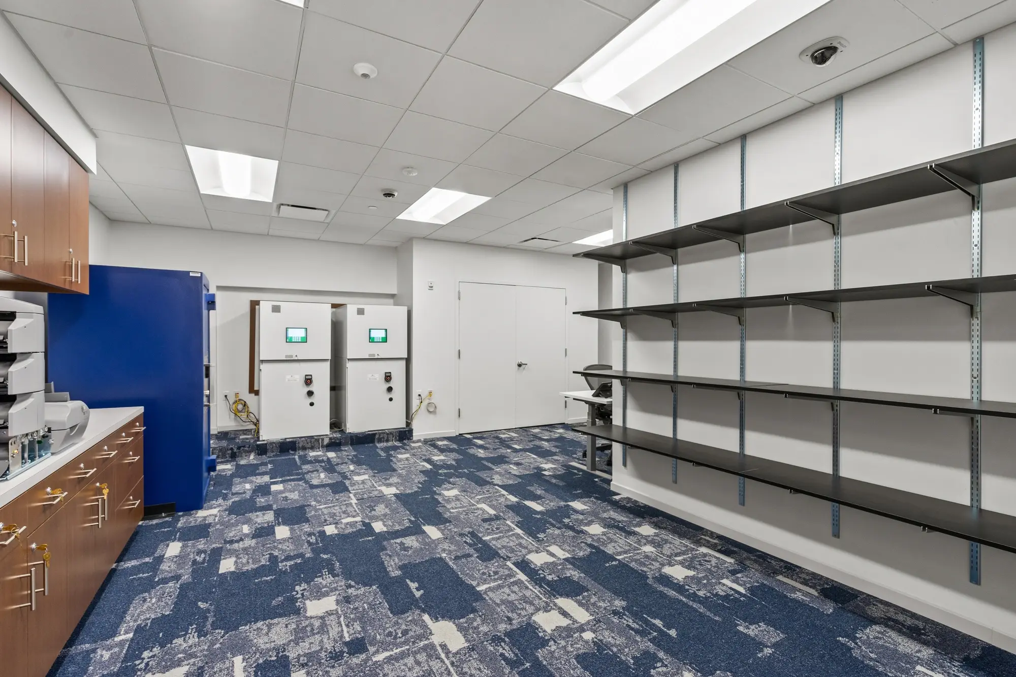 Secure storage and vault area with blue safe, oak cabinetry, metal shelving, and commercial-grade flooring