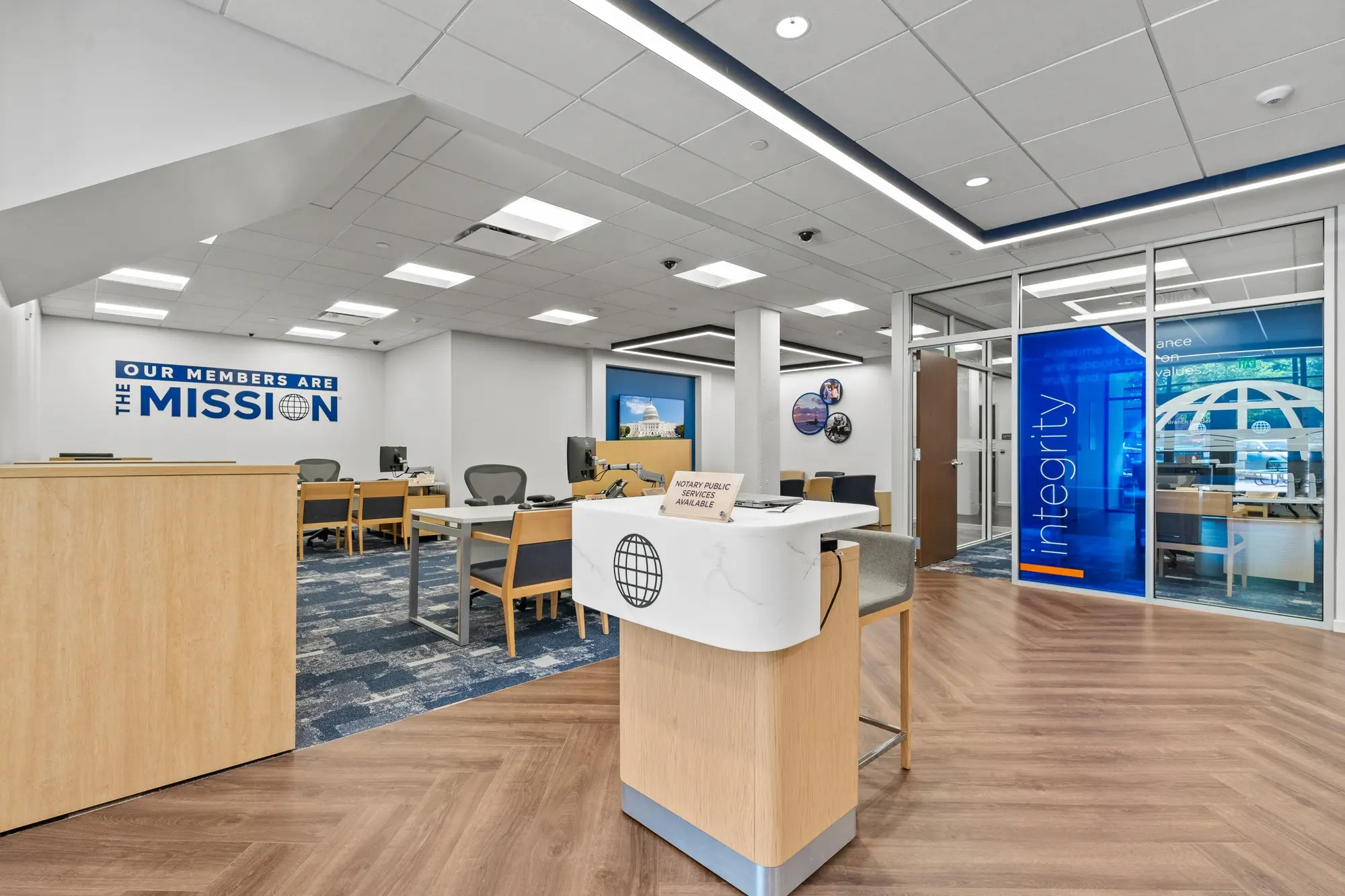 Open branch floor with greeter desk, advisor workstations, "Our Members Are The Mission" branding, and glass-walled integrity consultation room