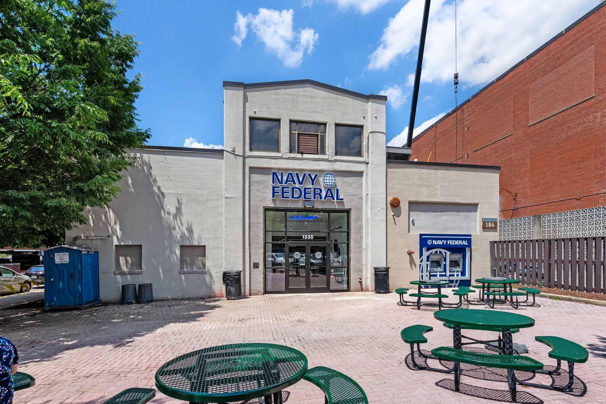 Wide exterior view of Navy Federal Credit Union DC branch with brick neighbor building and tree-lined patio