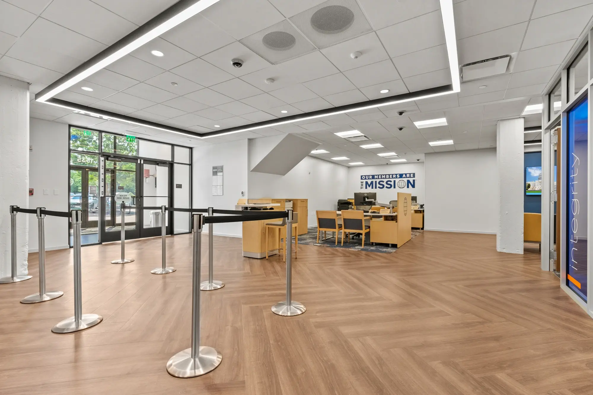 Branch interior viewed from entry doors showing open floor plan with stanchions, advisor desks, and "Integrity" branded consultation room