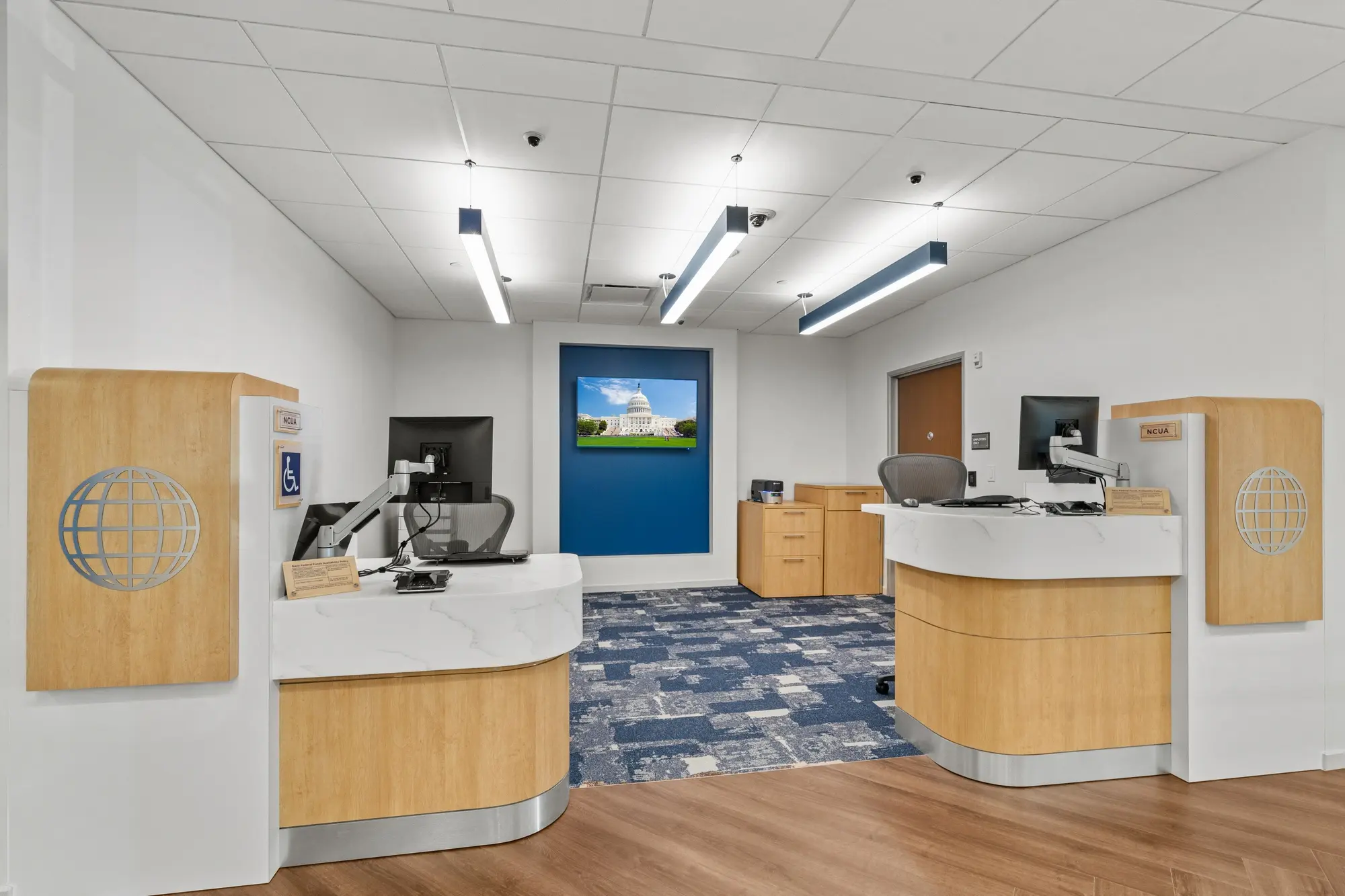 Dual teller stations with marble countertops, oak globe-logo privacy panels, Capitol Building display, and modern pendant lighting