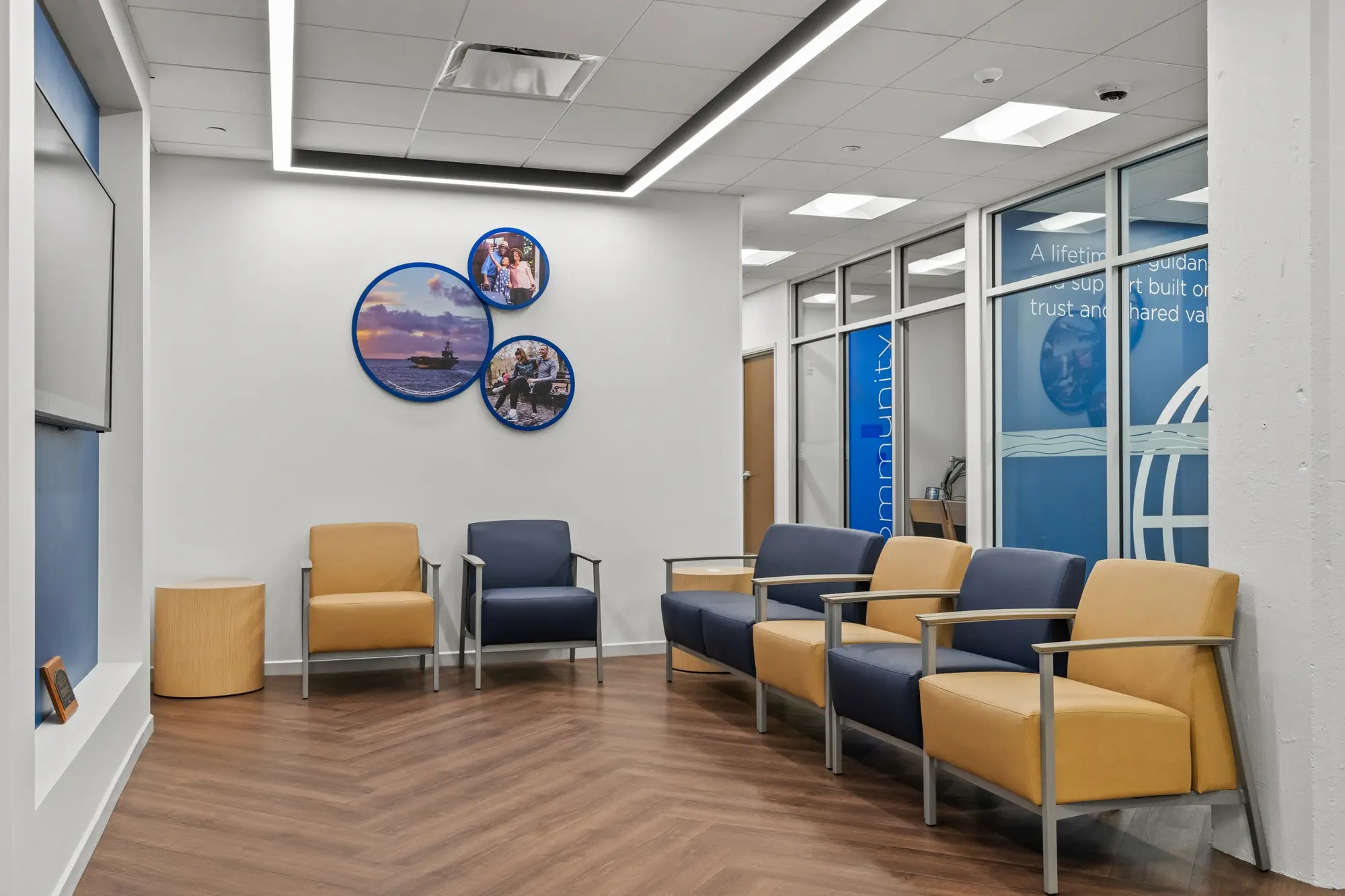 Member waiting area with navy and gold upholstered chairs, circular military family photo displays, and branded glass partition