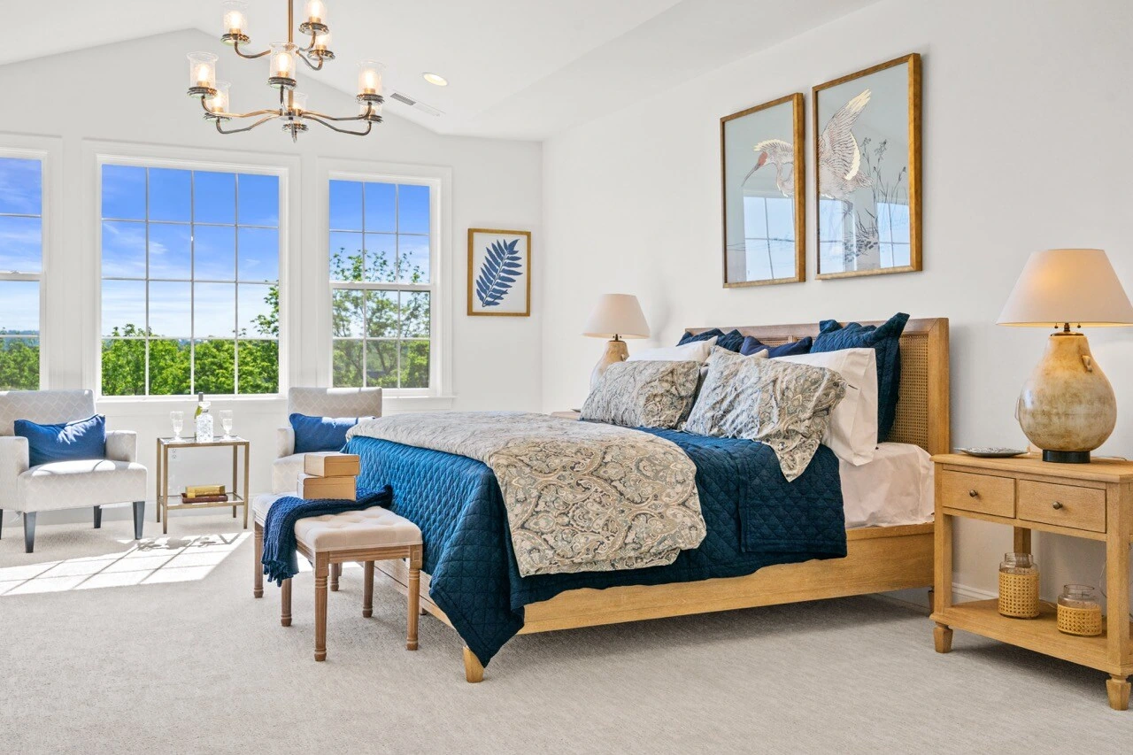 Bright primary bedroom with vaulted ceiling, blue bedding, chandelier, and nature artwork