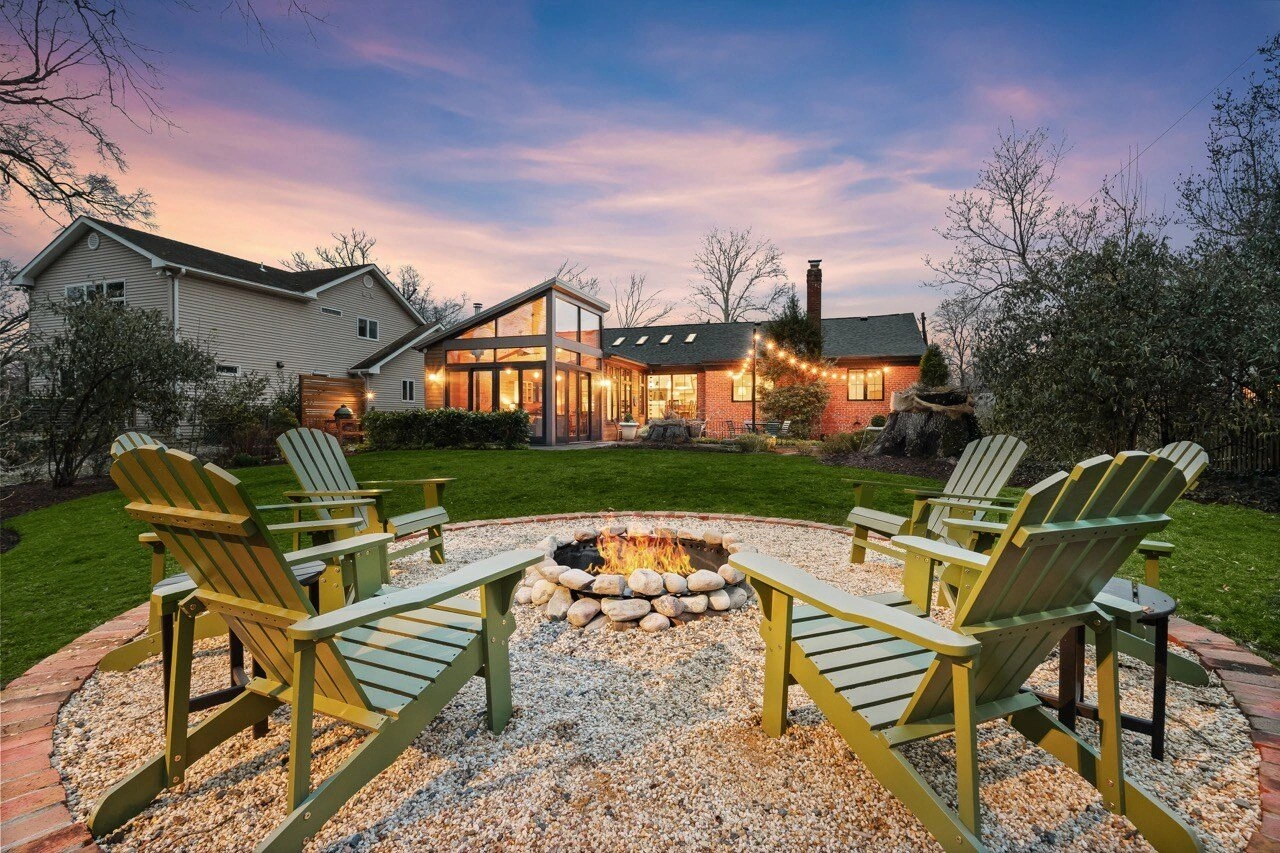 Twilight backyard with fire pit, Adirondack chairs, string lights, and screened porch